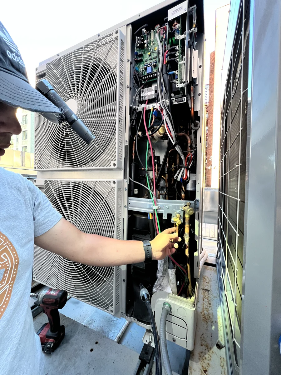 Technician checking service valves and the control board inside an opened VRF outdoor unit