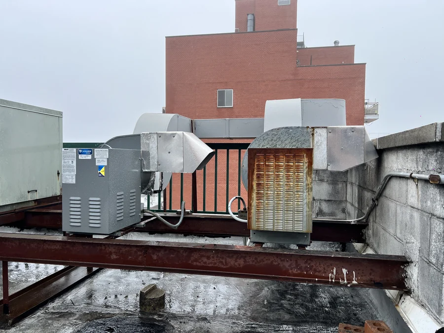 Rooftop exhaust blowers and ductwork with a corroded louvered intake, tagged during an exhaust fan survey