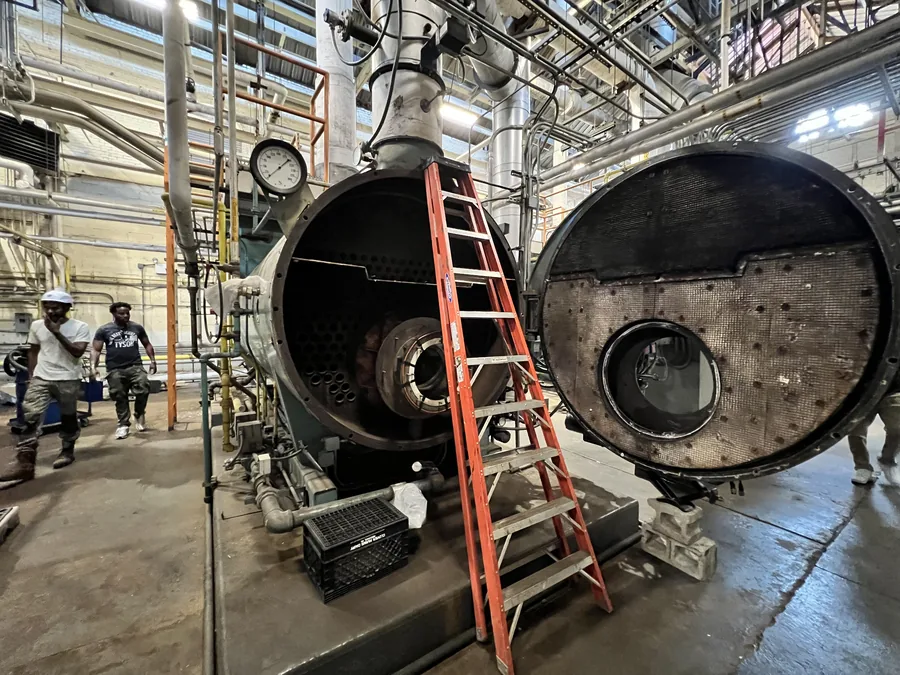 Technicians inspecting the tube sheet of an opened firetube boiler in a NYC plant room